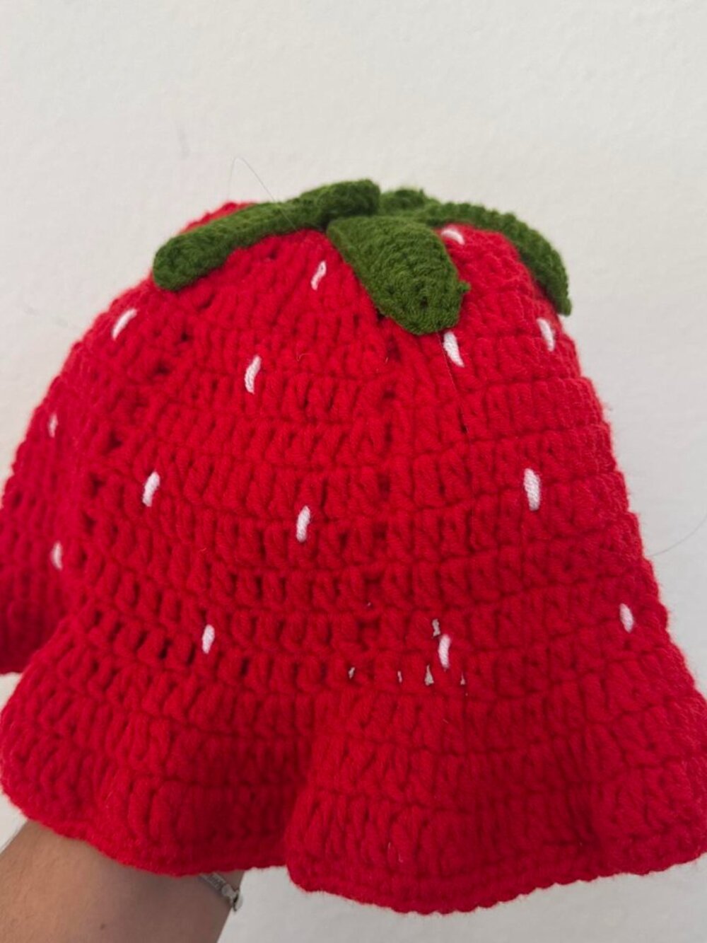 Red crochet strawberry hat with white seed details and green leaf top